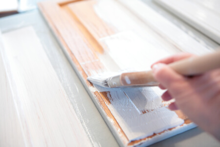 Person priming raw kitchen cabinet doors with a bristle brush