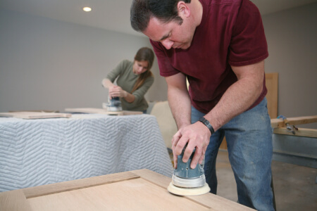 Two adults using orbital sanders to sand down kitchen cabinet doors