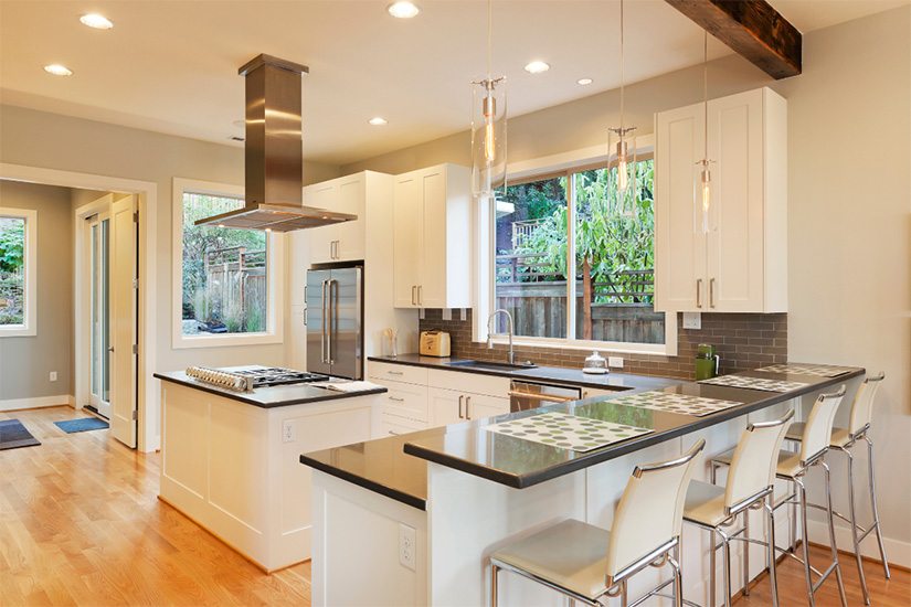 White shaker kitchen cabinets White shaker L-shaped industrial kitchen with gray quartz countertops, a wood beam and stainless-steel island hood.