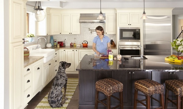 woman cooking at center island smiles at large dog sitting nearby in kitchen with cream raised panel cabinets on perimeter and dark furniture look island woman cooking at center island smiles at large dog sitting nearby in kitchen with cream raised panel cabinets on perimeter and dark furniture look island